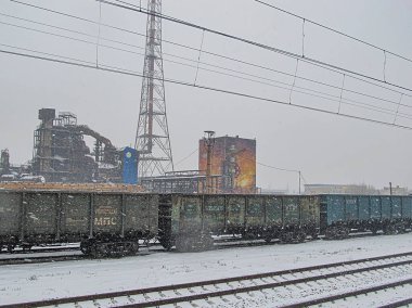 Eski bir fabrikanın önündeki elektrik hatlarına paralel, raylarda mavi bir trenin yer aldığı karlı bir sanayi sahnesi. Gökyüzü kapalı, bu da soğuk hava koşulları gösteriyor ki Kostiantynivka, Ukrayna, 01-15-2013