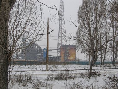 Görüntü, kışın harap olmuş fabrikası veya elektrik santrali, karla kaplı zemini, bulutlu gökyüzü, elektrik direkleriyle ve sessiz renk paleti Kostiantynivka, Ukrayna, 01-15-2013