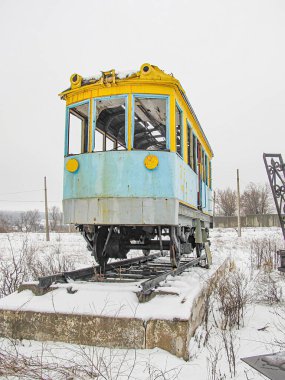 Geniş bir alanda karlı pistlerde eski, işlevsiz mavi ve sarı bir tramvay. Hava bulutlu ve hafif kar yağışlı Kostiantynivka, Ukrayna, 01-15-2013