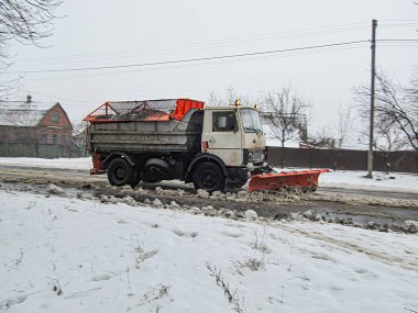 Görüntü, iki fotoğrafın birleşimini gösteriyor. Turuncu bir inşaat aracı, kar kaplı bir yola park etmiş ve Kostiantynivka, Ukrayna, 01-15-2013 için daha düşük bir fotoğrafta saban eklentisi var.