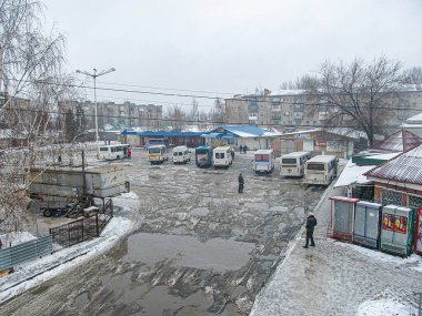 Park halindeki araçlar, durgun su ve gri bulutlu gökyüzünün altında çatıları karlı binaların arasında yürüyen bir kişi atmosfer şekeri Kostiantynivka, Ukrayna, 01-15-2013