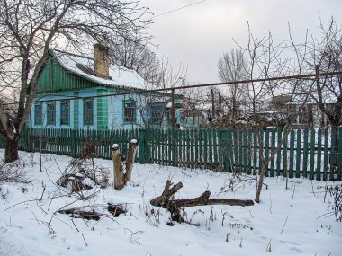 Açık mavi, tek katlı bir ev soğuk havada çatılı ve beyaz sazlıklarla çevrili, çıplak ağaçlar, kar ve çürüyen çitlerle çevrili sahne smal Kostiantynivka, Ukrayna, 01-15-2013