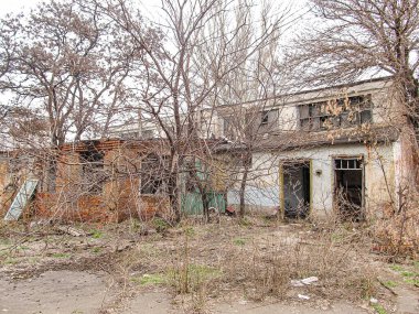 İki katlı terk edilmiş bir bina, kırık ya da tahta kaplı pencereler, çıplak ağaçlar, dağınık yabani otlar ve Kostiantynivka, Ukrayna, 06-15-2013