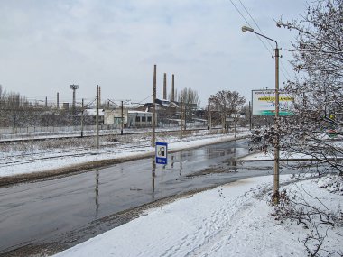 Bir kış sahnesinde kısmen karla kaplı bir şehir caddesi, kenarında küçük bir su birikintisi, sanayi bölgesinde yola paralel giden tren rayları, Kostiantynivka, Ukrayna, 01-15-2013