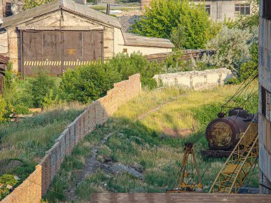 Raylarda eski, paslı bir tren vagonu, yangın çıkışlı yıpranmış bir bina ve Kostiantynivka, Ukrayna, 06-15-2013 'ü kısmen gizleyen uzun bir tuğla duvar ile kentsel bir manzaranın yüksek görüntüsü.