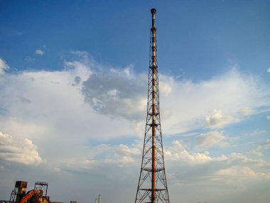 Görüntü, parçalı bulutlu gökyüzüne karşı çoklu kollara sahip metal bir anten kulesini gösteriyor. Borular, tanklar ve işleme ekipmanlarının yer aldığı sanayi tesisi, Kostiantynivka, Ukrayna, 06-15-2013
