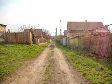 Görüntü, mütevazı evler ve yaprak döken ağaçların bulunduğu bir kentsel alanda terk edilmiş, asfaltsız bir yolu tasvir ediyor. Gökyüzü parçalı bulutlu Kostiantynivka, Ukrayna, 01-15-2013