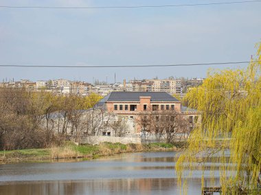 Geniş bir su kütlesi, bir bina, elektrik hatları ve bir ağaç ile sakin bir manzara görüntüsü sonbahar veya yaz sonu Kostiantynivka, Ukrayna, 01-15-2013