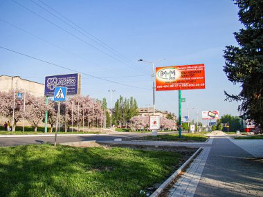 Asfaltlı yol, çimen medyanı, ağaçlar ve olası alışveriş merkezi veya ticari binası olan şehir gündüz sokak sahnesi bazı bulutlarla kaplı Kostiantynivka, Ukrayna, 06-15-2013