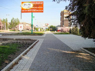 Görüntü, yeşillikle çevrili, muhtemelen bir yerleşim bölgesinde kentsel bir yürüyüş yolu olan açık hava ortamını gösteriyor. Arka planda kırmızı bir tabela var. Kostiantynivka, Ukrayna, 06-15-2013