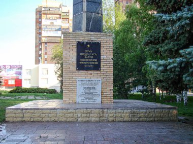 Dairesel bir vakıftaki hatıra plaketinin resmi, açık havada muhtemelen bir parkta yer alıyor. Plaketteki metinde Kostiantynivka, Ukrayna, 06-15-2013 tarihli KOBİ 'nin DEDICATED ve IN Anıları yazıyor.