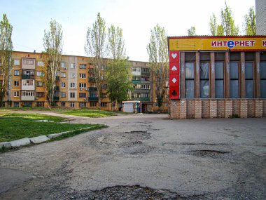 Görüntü, ilkbahar döneminde tam yapraklı ağaçlar, asfalt zeminli ve bazıları da Kostiantynivka, Ukrayna, 06-15-2013 tarihli samimi fotoğraflı, işaretli bir iskan binasını gösteriyor.