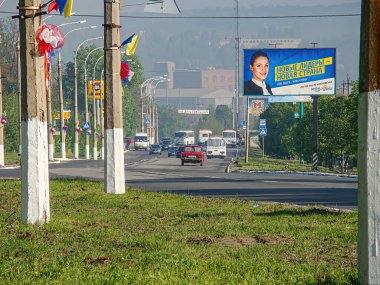 Görüntü, siyasi kampanya reklamları, ağaçlar, yeşillikler ve hareket eden araçların yer aldığı bir sokak sahnesini gösteriyor. Gökyüzü bulutlu Kostiantynivka, Ukrayna, 06-15-2013