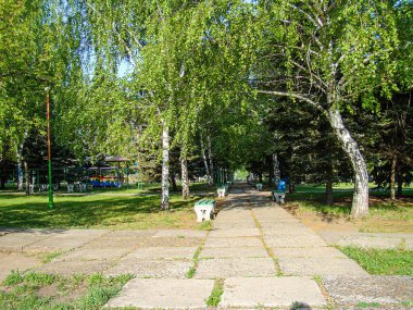 Görüntü, köşegen taş yolu, yemyeşil çimenler, ağaçlar, oyun alanı ve mavi bir sığınak içeren sakin bir park tasvir ediyor. Gökyüzü Kostiantynivka, Ukrayna, 06-15-2013