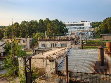 Gün batımında bir sanayi bölgesi, harap olmuş binalar, solan ışığı yansıtan büyük bir yapı, molozların arasında bitki örtüleri ve geçmişteki acti Kostiantynivka, Ukrayna, 06-15-2013