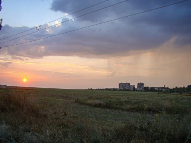 Otlak arazili sakin kırsal günbatımı sahnesi, uzaktaki binalar, elektrik hatları ve turuncudan mavi Kostiantynivka 'ya geçiş yapan güzel bir gökyüzü, Ukrayna, 06-15-2013