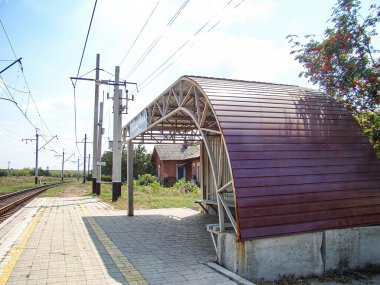 Kavisli metal sığınaklı tren istasyonu platformu, sarı güvenlik işaretleri, işaretli direk, kırsal-kırsal arka plan, boş platform, gündüz vakti Kostiantynivka, Ukrayna, 06-15-2013