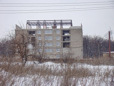 Görüntü, çok katlı bir inşaat alanı, beton duvarlar, çelik kirişler, vinç ve karlı zemin ağaçlarının ön planda yaprakları olmayan Kostiantynivka, Ukrayna, 01-15-2013