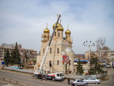 Bir resimde, kentte, park halindeki arabalar, ağaçlar, Kostiantynivka, Ukrayna, 01-15-2013 tarihli özel soğan şekilli kubbeleri ve bakımlı altın haçları olan süslü bir Doğu Ortodoks kilisesi görülüyor.