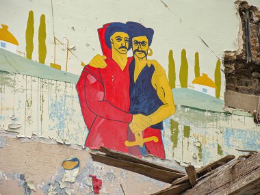 Geleneksel giyinmiş, kucaklayan, sıkıntılı bir arkaplan karşısında canlı renklerle boyanmış iki adamı resmeden bir duvar resmi halk sanatı Kostiantynivka, Ukrayna, 01-15-2013