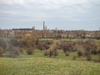 Muhtemelen sonbahar veya kış aylarında çekilen çıplak ağaçlarla kaplı açık bir arazinin siyah-beyaz manzara fotoğrafı, Kostiantynivka, Ukrayna, 01-15-2013 uzun yapıları olan bir endüstriyel kompleksi içeriyor.