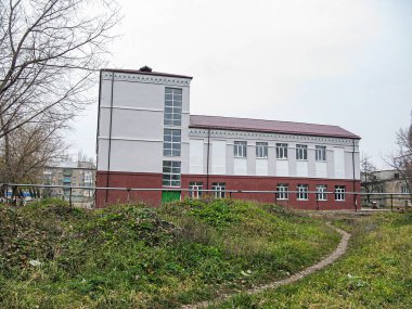 Gri üst ve kırmızı tuğlalı alt parçaları, beyaz veya yeşil çerçeveli birden fazla penceresi olan iki katlı bir bina, girişin üzerinde bir çıkıntı, Kostiantynivka, Ukrayna 'ya giden kirli bir yol, 06-15-2013