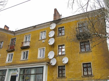 Görüntü çok katlı bir binanın ön cephesinde uydu antenleri, bulutlu bir gökyüzünün altında binaların kapalı perdeleri ve jaluzileri ve Kostiantynivka, Ukrayna, 06-15-2013 işaretleri var.