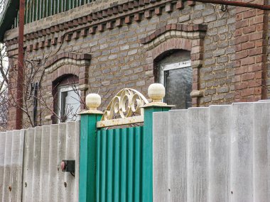Görüntü tuğla duvarları, penceresi ve metal kapısı olan bir konutu gösteriyor. Ev kapalı bir günde Kostiantynivka, Ukrayna, 06-15-2013 'te boyalı bir çitle çevrili.
