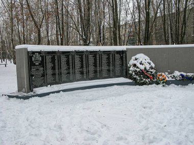 Kar kaplı, gri beton bir duvarda belirsiz bir yazı bulunan metal bir plakete suni çiçek çelengi eşlik ediyor. Kostiantynivka, Ukrayna 'da yapraksız ağaçlar, 01-15-2013