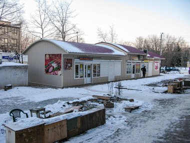 Bir kış mağazasının önündeki manzara, karla kaplı çatı ve zemin ile soğuk hava giysileri içinde bir kişi binaya doğru yürüyor. Gökyüzü bulutlu, yürüyüş alanı temizlenmiş, Kostiantynivka, Ukrayna, 01-15-2013
