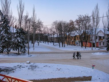 Karlı, bulutlu bir sokakta kış manzarası, yürüyen iki kişi, binalar, küçük mağazalar, çıplak ağaçlar, araç rayları Kostiantynivka, Ukrayna, 01-15-2013