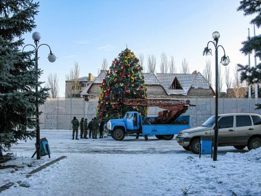 Bir grup birey dışarıda süslü bir Noel ağacı kuruyor, muhtemelen bir şehir meydanında ya da parkta, karlı zeminde bir kamyon ve araba ile Kostiantynivka, Ukrayna, 01-15-2013