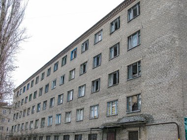 Pencereli çok katlı tuğla bir bina, bazıları kısmen kapalı ve diğerleri kısmen açık bulutlu bir günde alt pencerelerden birinde bir kişi görülüyor The Kostiantynivka, Ukrayna, 01-15-2013