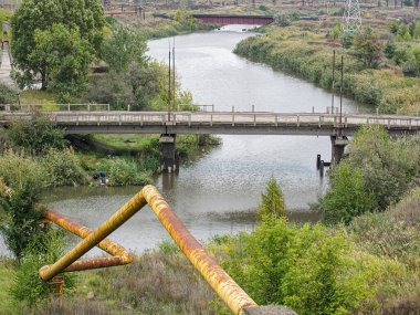 Görüntü, bulutlu bir gökyüzü altında Weir, köprü, bitki örtüsü ve sanayi yapılarına sahip bir nehri gösteriyor. Kostiantynivka, Ukrayna, 06-15-2013