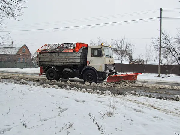 Görüntü, iki fotoğrafın birleşimini gösteriyor. Turuncu bir inşaat aracı, kar kaplı bir yola park etmiş ve Kostiantynivka, Ukrayna, 01-15-2013 için daha düşük bir fotoğrafta saban eklentisi var.