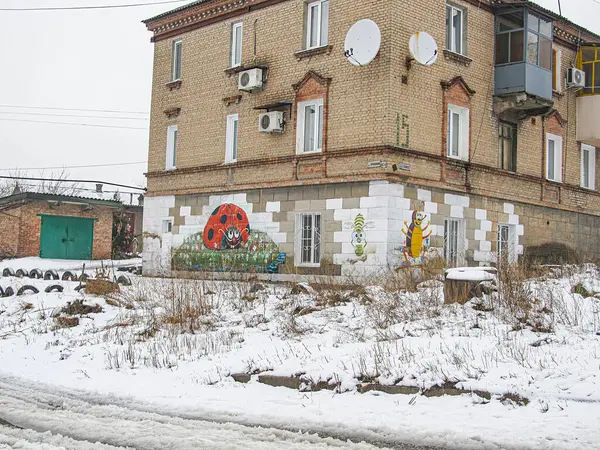 Birden fazla penceresi olan tuğla bir bina, beyaz çerçeveli veya çerçevesiz, çatıda bir uydu anteni, ve antropomorfik bir figürü resmeden graffiti sanatı Snow siyah Kostiantynivka, Ukrayna, 01-15-2013