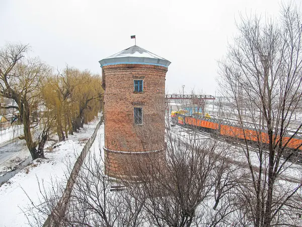 Sağlam tuğlalı bir yapısı, karlı zemini, ağaçlı ve uzak köprüsü olan yakındaki su, arka planda hareket eden tren, bulutlu gökyüzü Kostiantynivka, Ukrayna, 01-15-2013