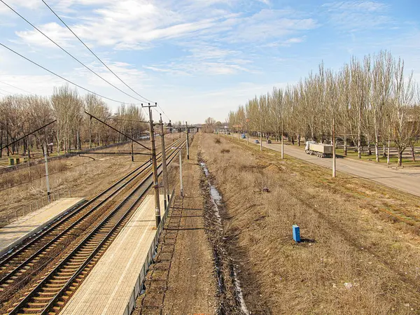 Çimenler ve çıplak ağaçlarla çevrili terk edilmiş bir demiryolu hattı, sol tarafta görünür bir elektrik hattı yapısı ile raylar yakın zamanda Kostiantynivka, Ukrayna, 06-15-2013