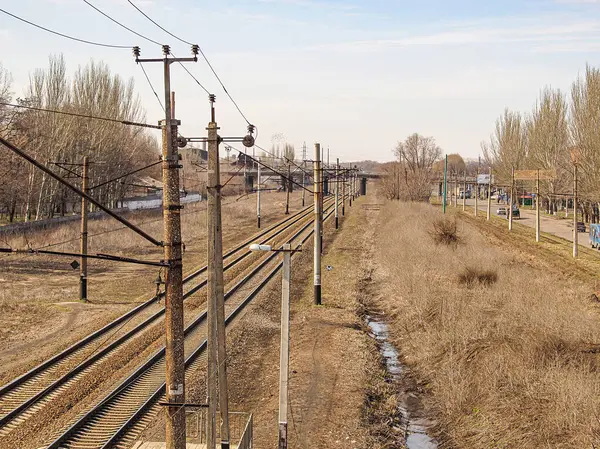 Elektrikli bir demiryolu hattı, çıplak ağaçlar ve üstten kablolarla çevrili kırsal ya da yarı kentsel bir arazi boyunca uzanır. Açık gökyüzü, Kostiantynivka, Ukrayna, 01-15-2013