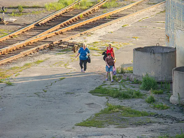 Eski bir tren yolunda koşan üç kişi, koyu ve açık renk giyinmiş sahne terk edilmiş görünüyor. Aşırı gelişmiş bitki örtüsü, çelik raylar, tahta yataklı Kostiantynivka, Ukrayna, 06-15-2013
