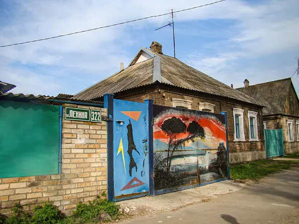 Görüntü, muhtemelen düşük gelirli veya endüstriyel bir alanda yıpranmış mavi bir kapı ve canlı bir grafiti ile kentsel bir açık hava sahnesini gösteriyor. Grafiti bir siluet Kostiantynivka, Ukrayna, 06-15-2013