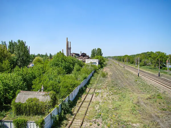 Ukrayna 'nın Kostiantynivka kentinde sakin bir günde ön planda harap bir bina bulunan bitkilerle çevrili uzak bir demiryolu hattının fotoğrafı. 06-15-2013