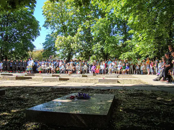 Bir mezarlık veya anıt alanında küçük taşlarla çevrili merkezi bir taş plaketle yapılan bir anma töreninde kalabalık, Kostiantynivka, Ukrayna, 06-15-2013 yıllarında düzenlenen etkinlikte dikkatle ayakta duruyor.