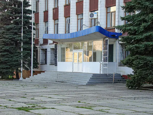 Beyaz kaplamalı, çok katlı, koyu kırmızı pencere elementleri ve düz çatısı olan bir bina girişte mavi çizgili bir tente var, merdivenler yukarı çıkıyor, Kostiantynivka, Ukrayna, 06-15-2013