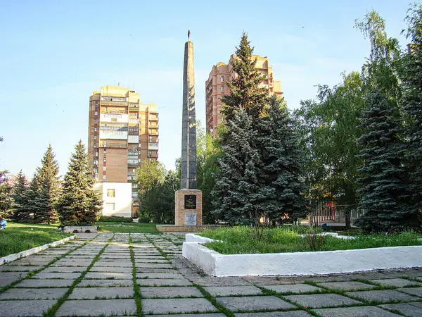 Merkezi bir taş dikilitaşlı, asfalt kaldırımlı, alçak beyaz duvarı çevreleyen huzur parkı veya arka planda Lush Evergreen ağaçları ve kentsel binalar, c Kostiantynivka, Ukrayna, 06-15-2013