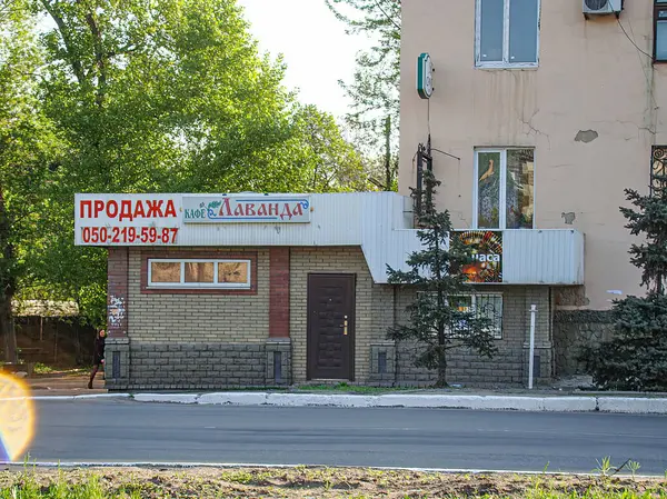 Daha soğuk hava koşulları altında gıda kuruluşunun görüntüsü. Tenteli, yakındaki ağaçlı ve bulutlu basit metal bina. Kostiantynivka, Ukrayna, 06-15-2013