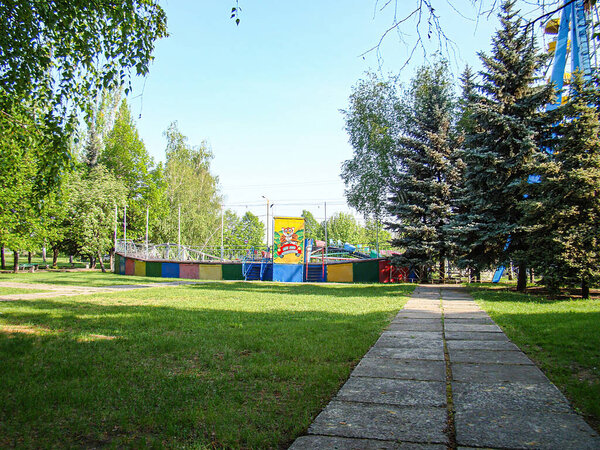 Живая парковая сцена с красочной детской площадкой, каменной дорожкой, деревьями и ясным небом Константиновка, Украина, 06-15-2013