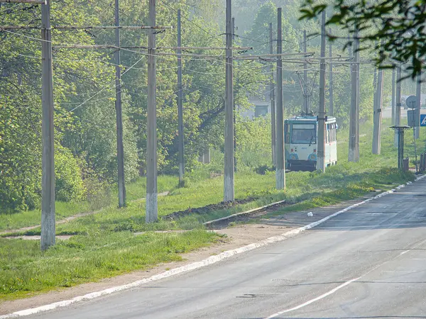 Görüntü, yağmurdan ıslanmış, elektrik tramvayı uzaklaşıyor, elektrik hatları, yüksek ağaçlar ve çimenli bir alan içeren bir sokak sahnesi gösteriyor. Yumuşak ışık Kostiantynivka, Ukrayna, 06-15-2013