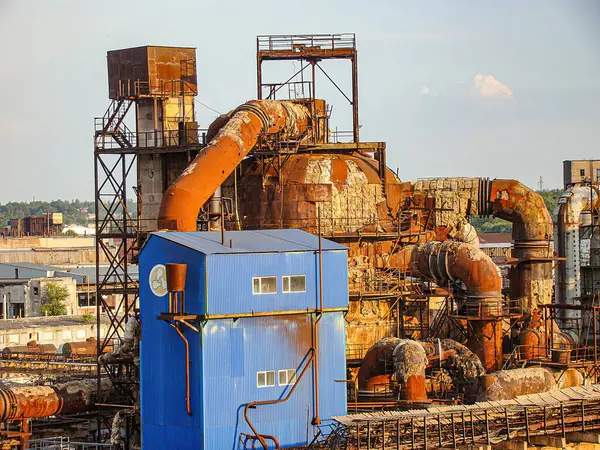 Uzun tuğla baca, havalandırma boruları ve çeşitli paslı yapılara sahip eski endüstriyel bir kompleksin görüntüsü açık bir gökyüzü ve yeşil ve Kostiantynivka, Ukrayna, 06-15-2013
