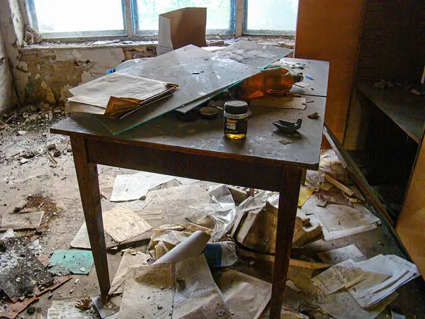 Düzensiz çalışma alanı dağınık masa, açık kitap, renkli kavanozlar sarı, mavi, çıplak beton duvarlar, pencere, kullanılmayan kağıtlar, döküntüler ve ihmal hissi ve Kostiantynivka, Ukrayna, 06-15-2013